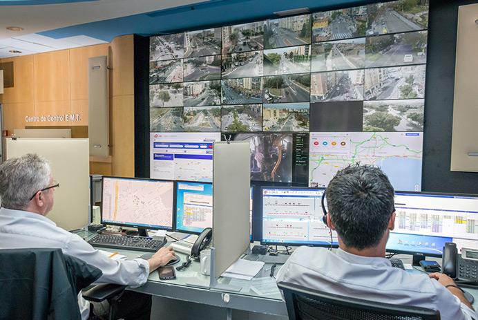 Sala de controle EMT Madrid com dois trabalhadores monitorando estradas e dados exibidos em uma parede de vídeo