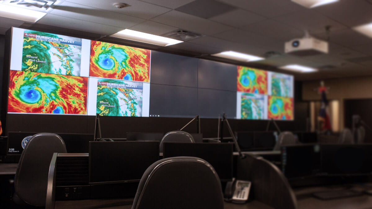 Sala de controle vazia com radares meteorológicos exibidos em uma grande parede de vídeo, e estações de trabalho