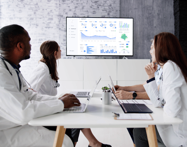 Médicos reunidos em uma sala de reuniões para analisar o painel de dados na tela