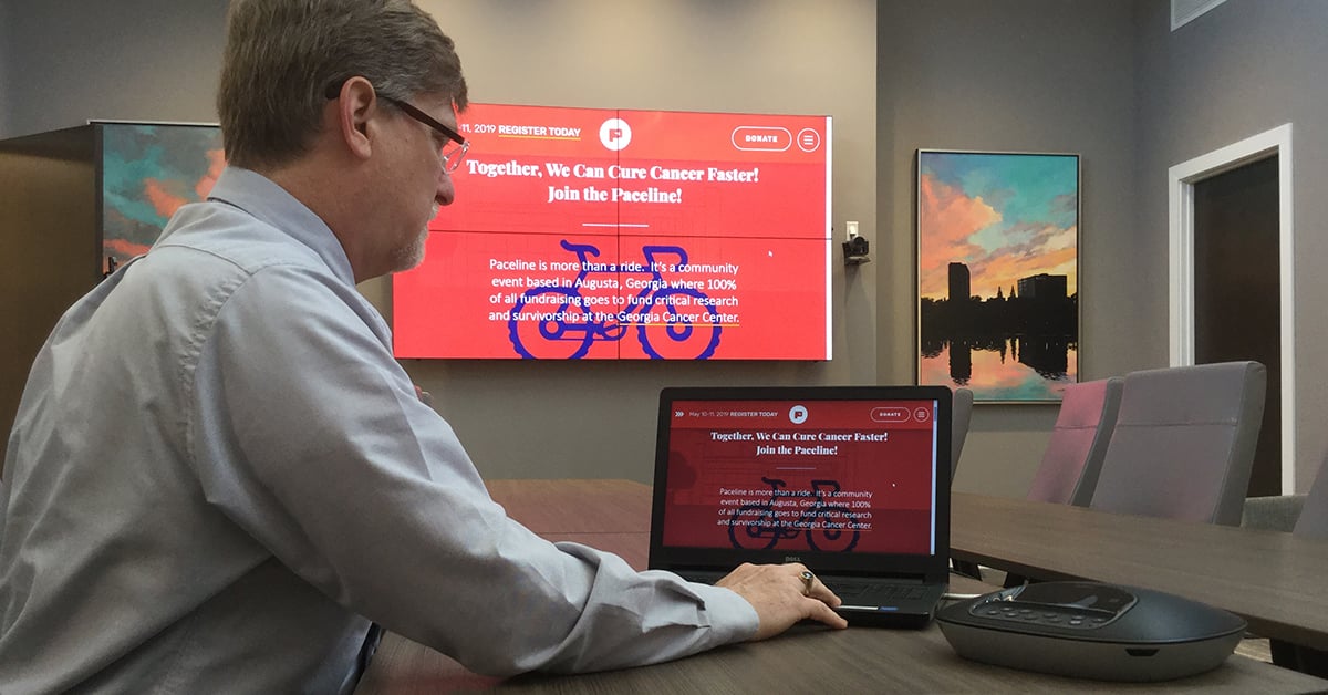 Sala de reuniões da Medical College of Georgia, com um homem usando seu laptop e Userful para exibir uma página da web em uma parede de vídeo atrás dele