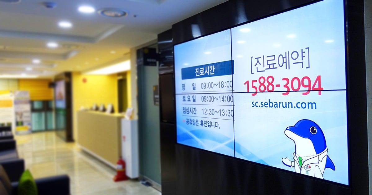 Área de espera do Seocho Se Barun Hospital, com parede de vídeo exibindo os horários e detalhes de contato