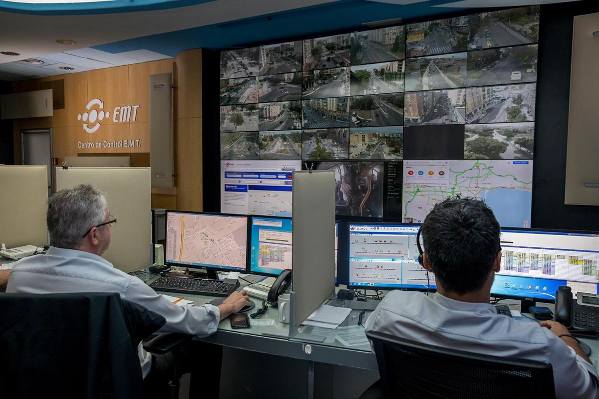 Centro de Controle EMT com trabalhadores monitorando as condições de trânsito através de suas estações de trabalho e uma parede de vídeo mostrando rotas de trânsito, filmagens ao vivo e dados