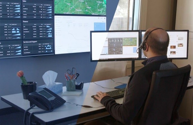 Funcionário na sala de controle em sua mesa de trabalho digitando, olhando para uma parede de vídeo exibindo painéis de dados e mapas