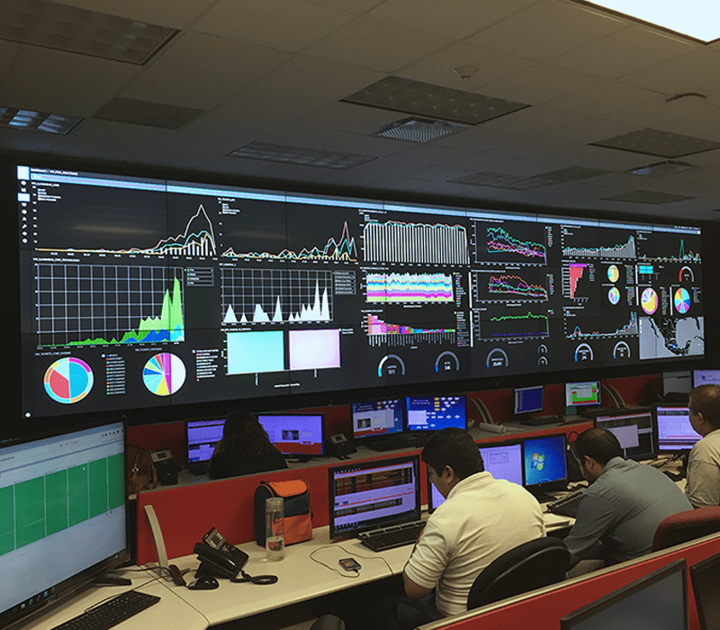 Funcionários que trabalham em uma sala de controle em estações de trabalho com paredes de vídeo exibindo painéis de dados