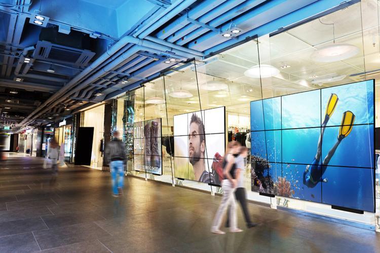 Múltiplas grandes paredes de vídeo em um corredor de shopping center, exibindo anúncios e arte