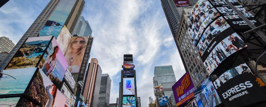 Times Square, em Nova York, cheia de paredes de vídeo e sinalização digital, e muitas pessoas durante o dia