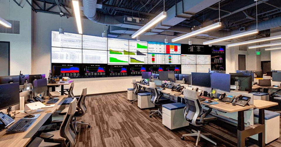 Centro de Operações de Rede Vazio SpectrumVoIP com muitas estações de trabalho e uma parede de vídeo maior exibindo painéis de dados